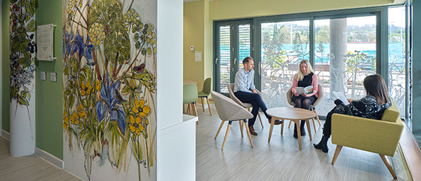 Cancer centre staff sitting in the wellbeing hub which is decorated with murals of flowers and comfortable furniture