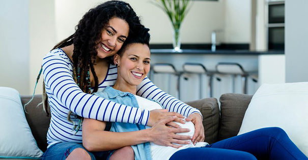Two smiling women, one holding the pregnant woman's bump