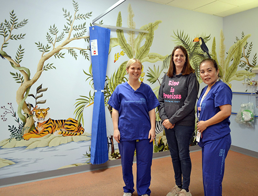 RUH staff and charity representitive standing in front of the mural which depicts and jungle scene with animals