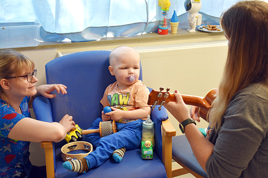 Young patient listens to our music therapist playing the ukulele