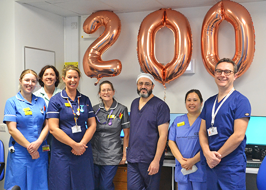 The hand surgery team standing in front of balloons spelling out the number 200